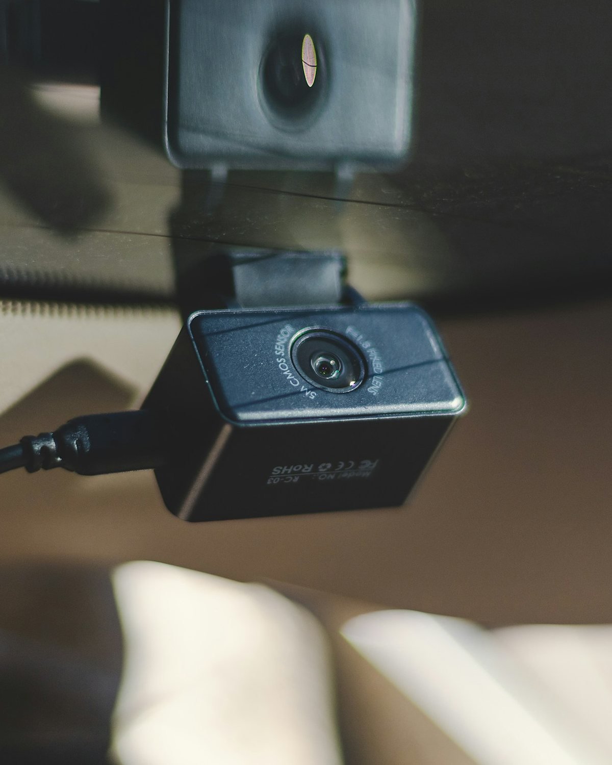 Small black dash camera hanging from a mount stuck to car glass, with a power cable plugged into its side