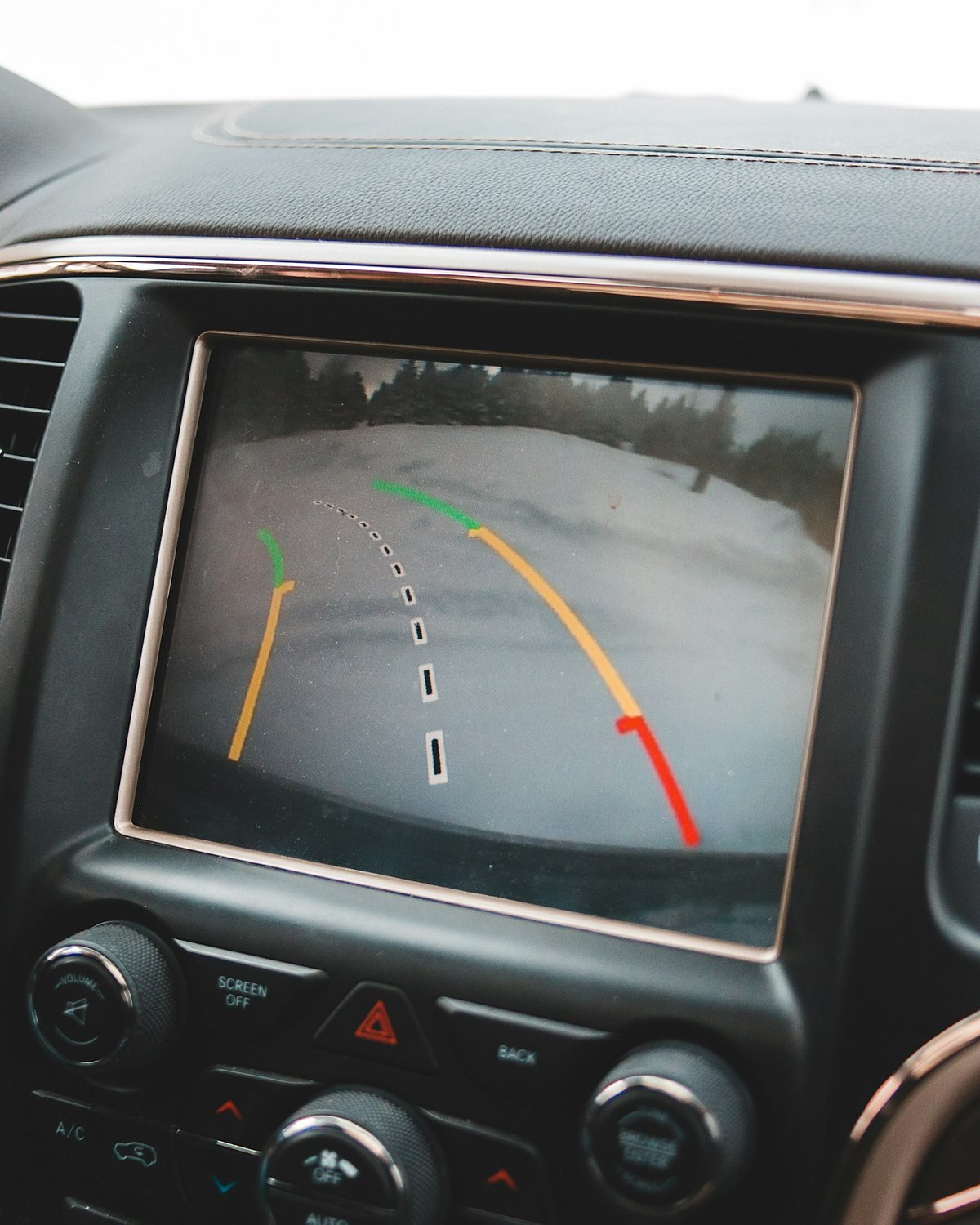 Car dashboard screen showing a rear camera view with coloured parking guide lines