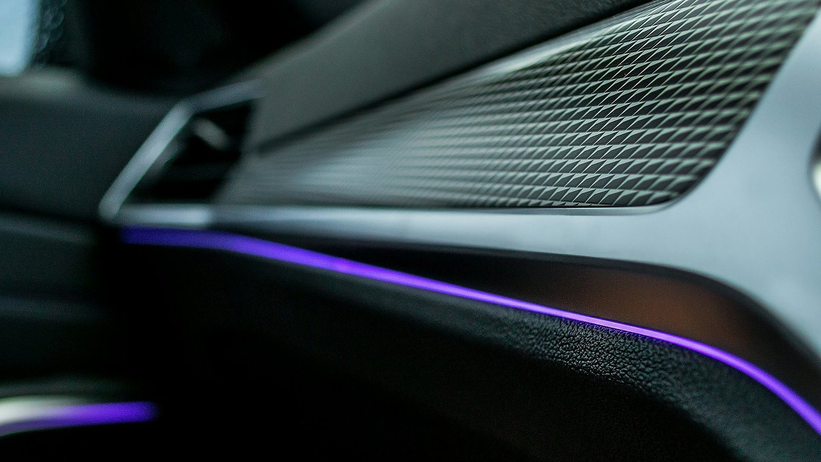 Close-up of a car dashboard with a textured trim panel and a purple ambient light strip