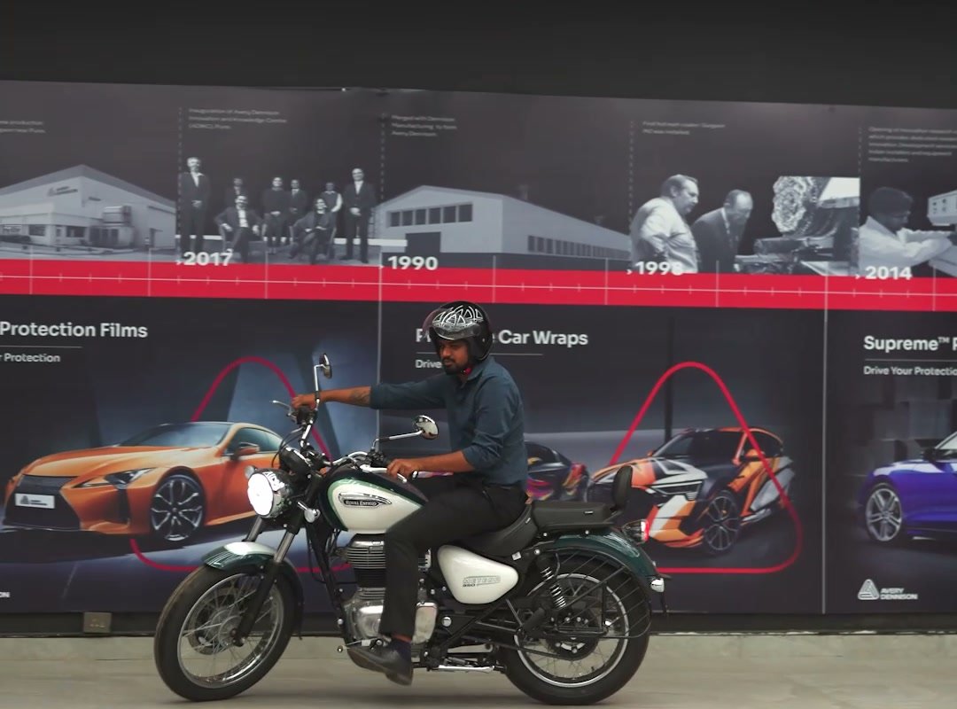 A rider on a Royal Enfield in front of the Avery Dennison timeline wall inside the studio.