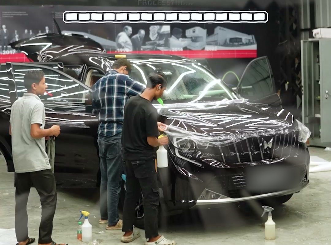 Installers laying clear film over the bonnet of a dark Mahindra SUV.