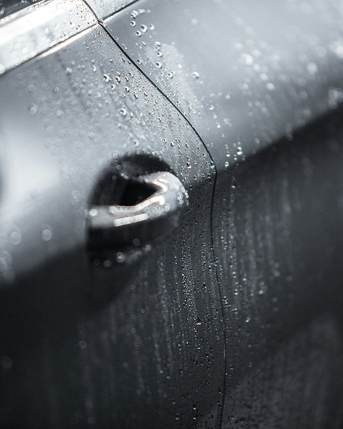 Water droplets on a dark grey car door beside the door handle and panel shut line