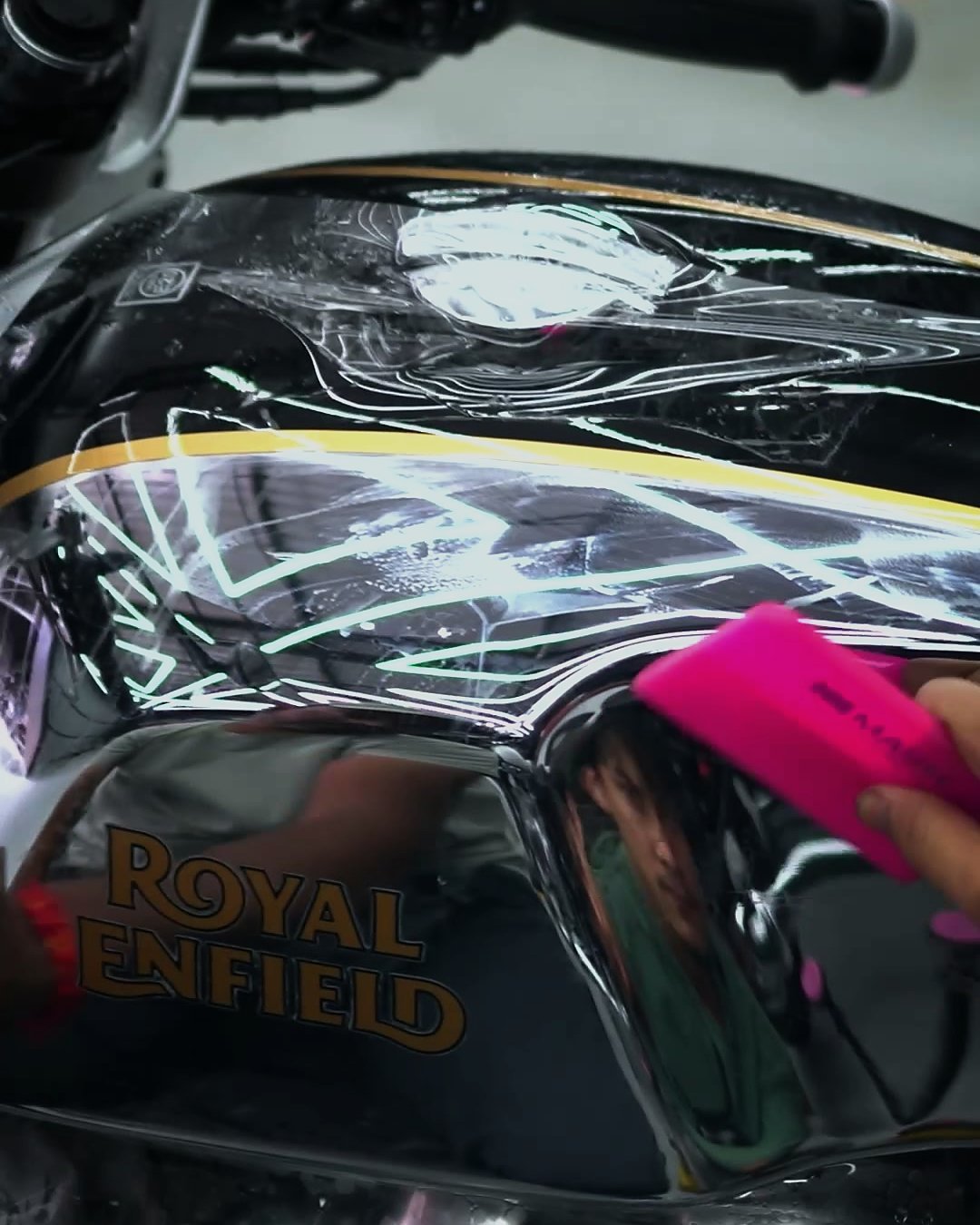 An installer pressing clear film onto the chrome tank of a Royal Enfield Continental GT 650 with a pink applicator.