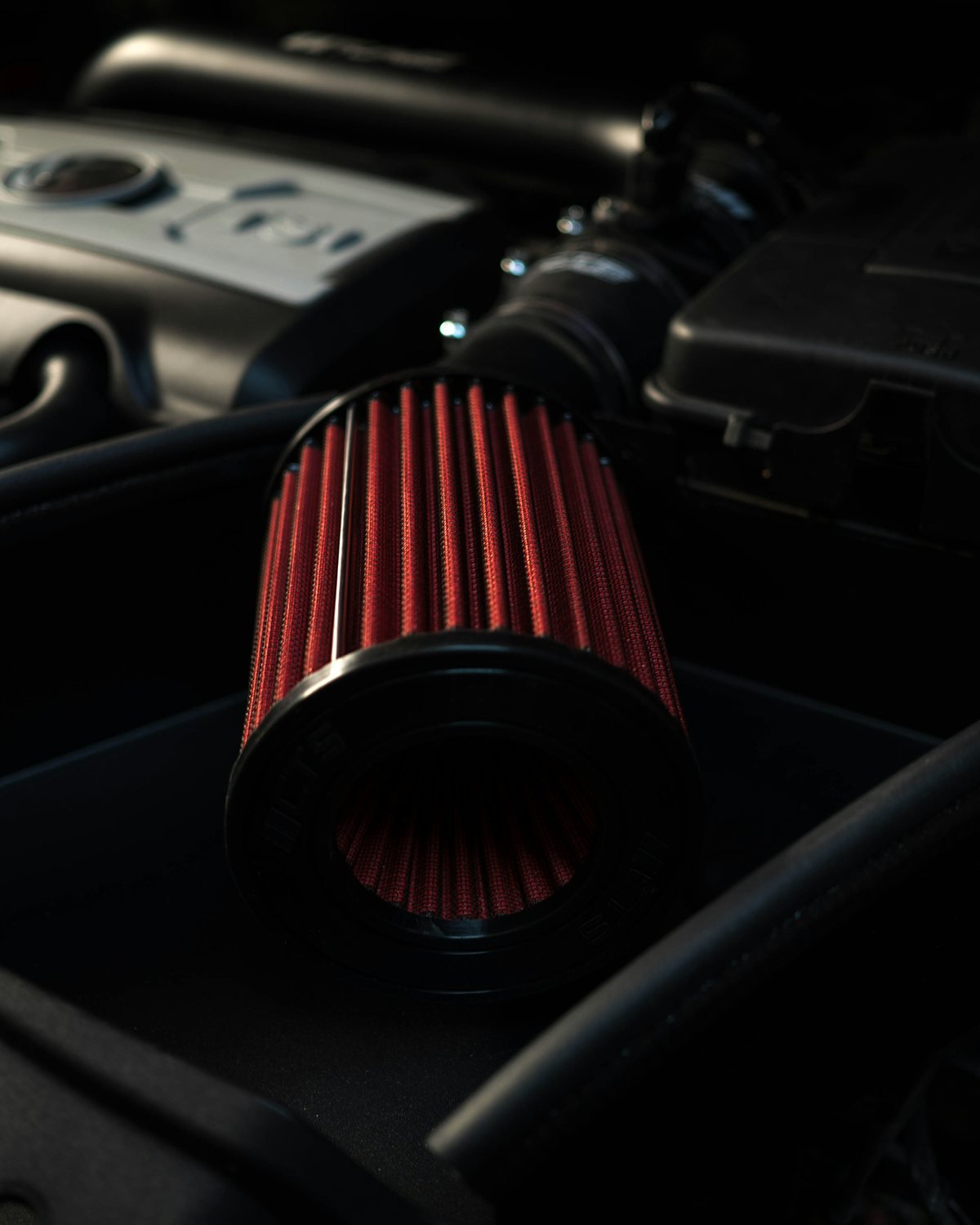 Red cone shaped air filter fitted to an intake pipe in a dimly lit engine bay