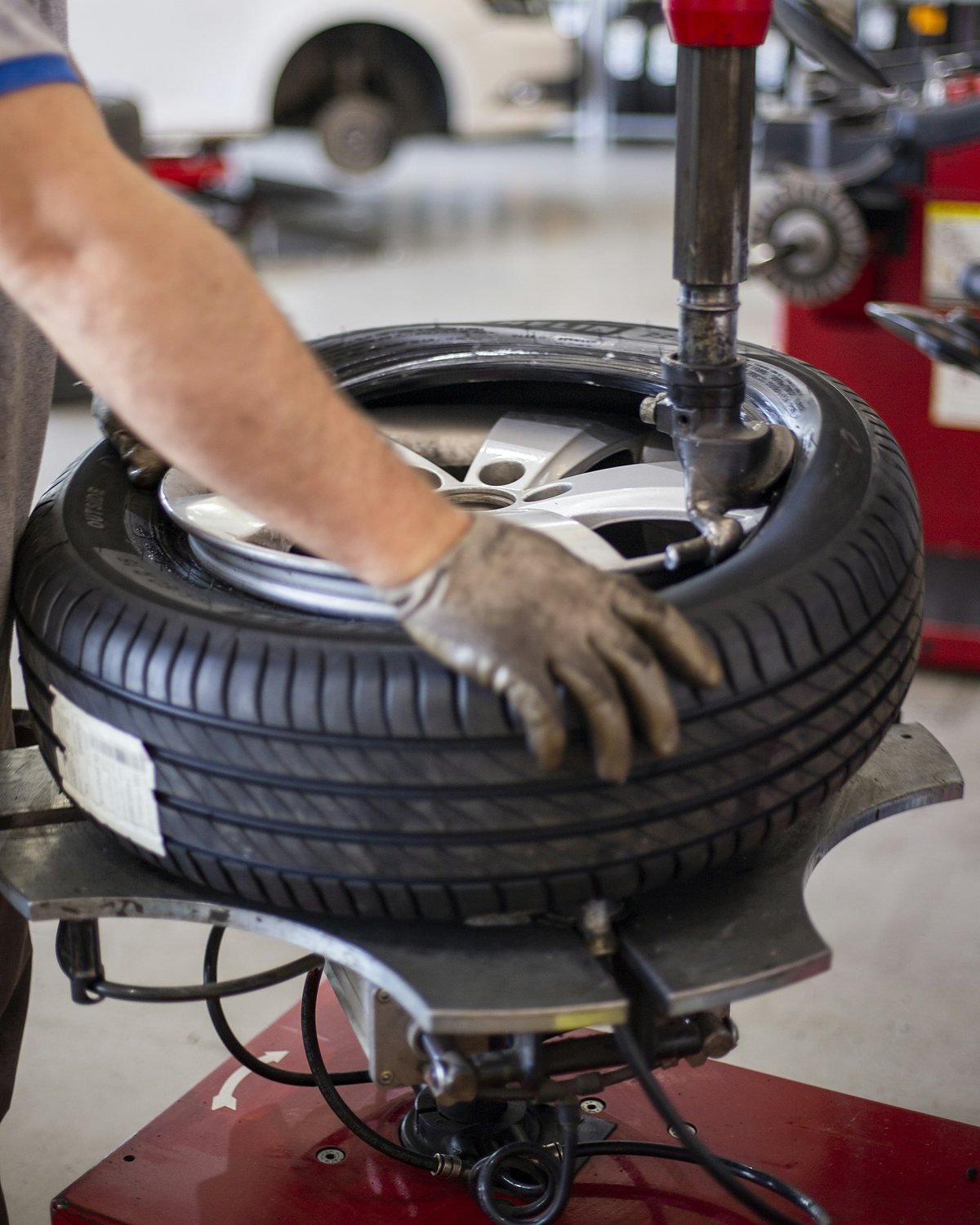 A gloved hand pressing on a tyre fitted to an alloy wheel on a tyre changing machine in a workshop