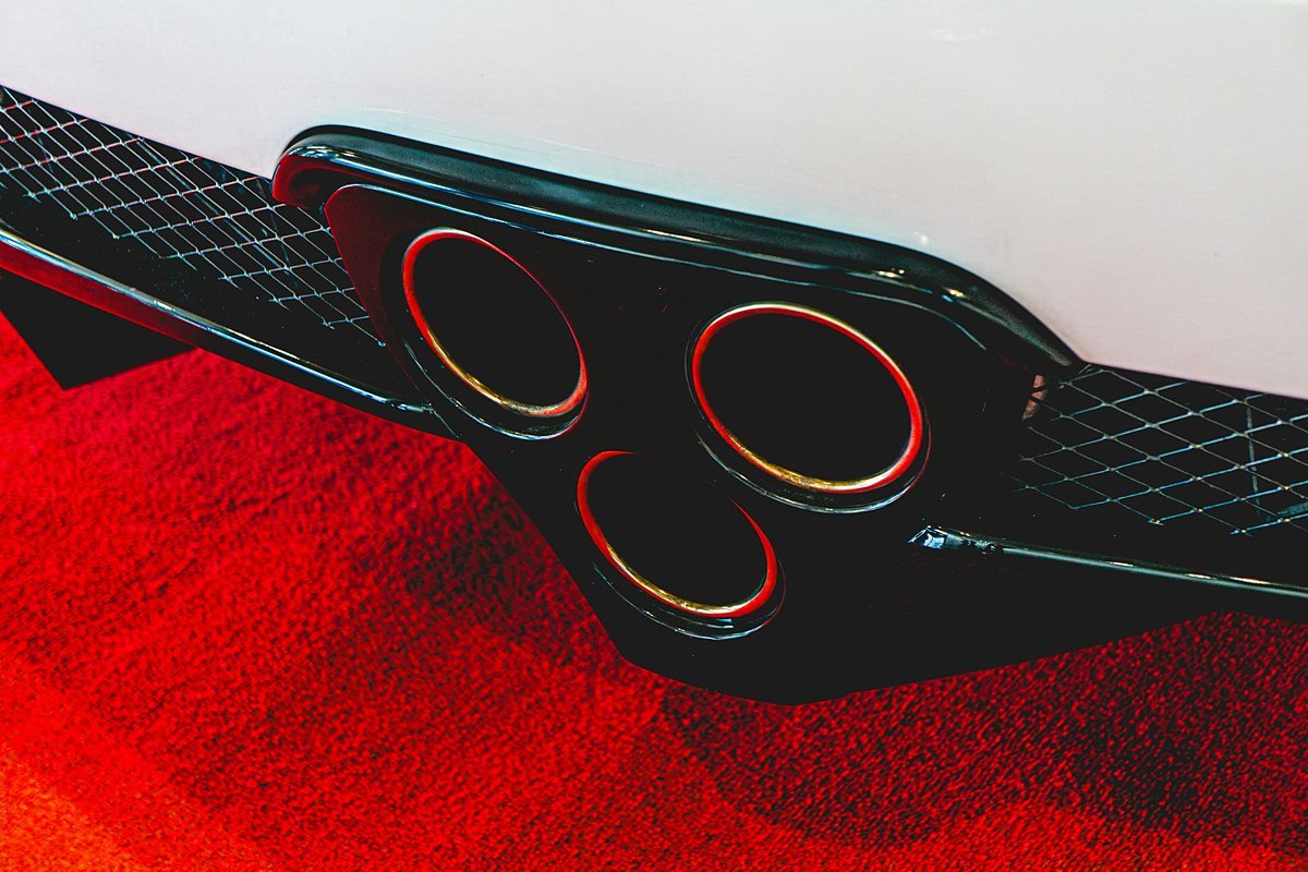 Three round exhaust tips in a gloss black rear diffuser with mesh vents on both sides, below a white bumper
