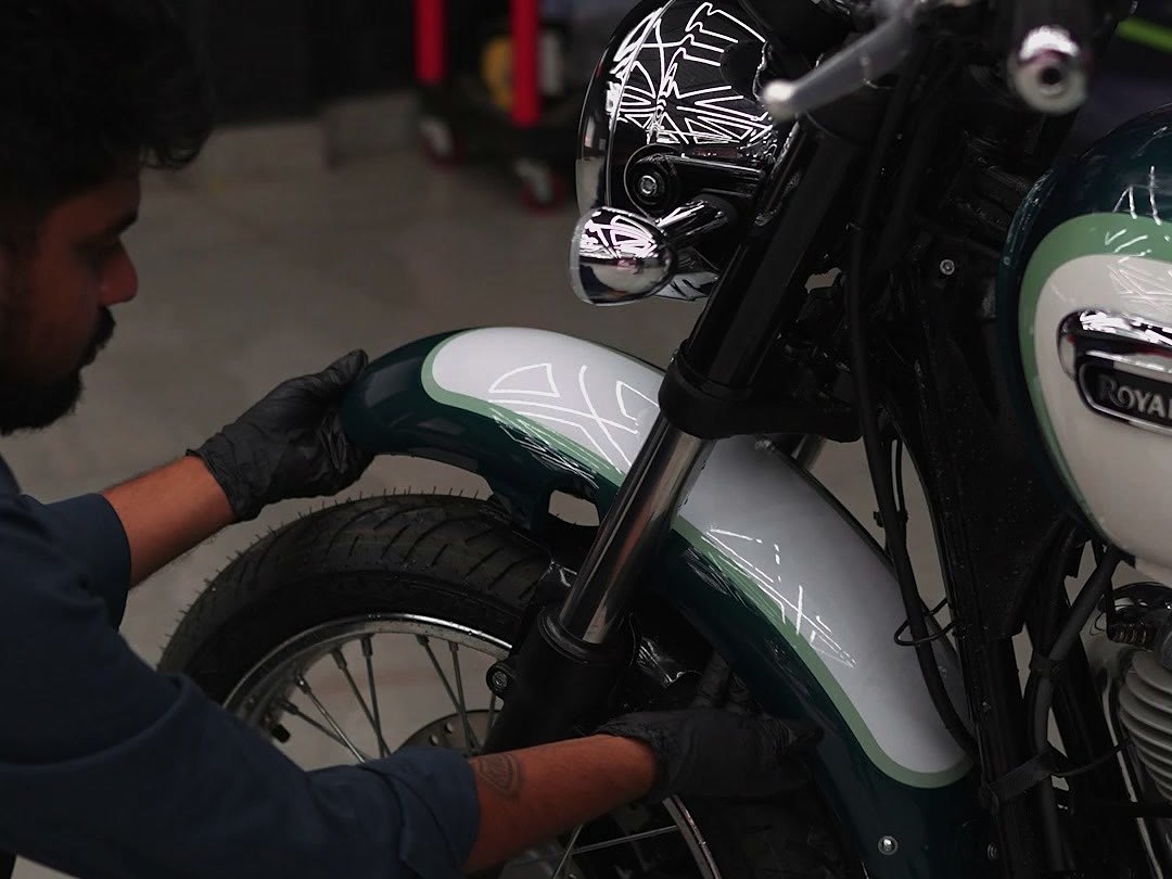 A technician in black gloves working on the front mudguard of a motorcycle.