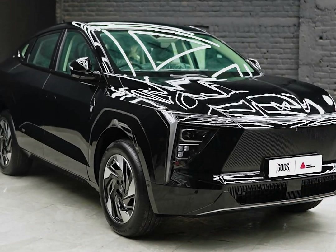 Black Mahindra XEV 9e from the front, with the studio grid reflected in the bonnet.